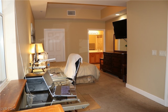 carpeted bedroom with a tray ceiling and connected bathroom