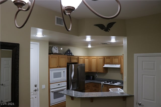 kitchen with kitchen peninsula, white appliances, stone counters, and a breakfast bar