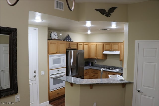 kitchen featuring white appliances, a breakfast bar area, light stone countertops, and kitchen peninsula