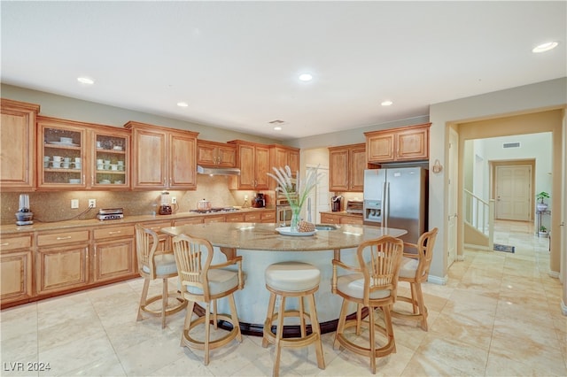 kitchen featuring a kitchen island, light stone countertops, stainless steel appliances, tasteful backsplash, and a kitchen bar