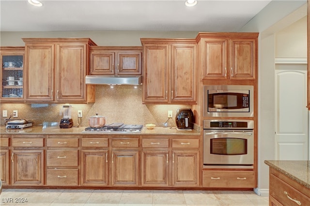 kitchen with light stone countertops, appliances with stainless steel finishes, light tile patterned floors, and tasteful backsplash