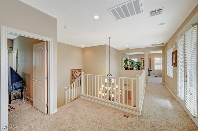 corridor with light colored carpet and a chandelier