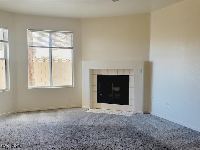 unfurnished living room featuring a tiled fireplace, baseboards, and carpet floors