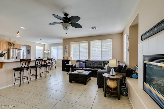 living room featuring light tile patterned flooring, ceiling fan with notable chandelier, and a tiled fireplace