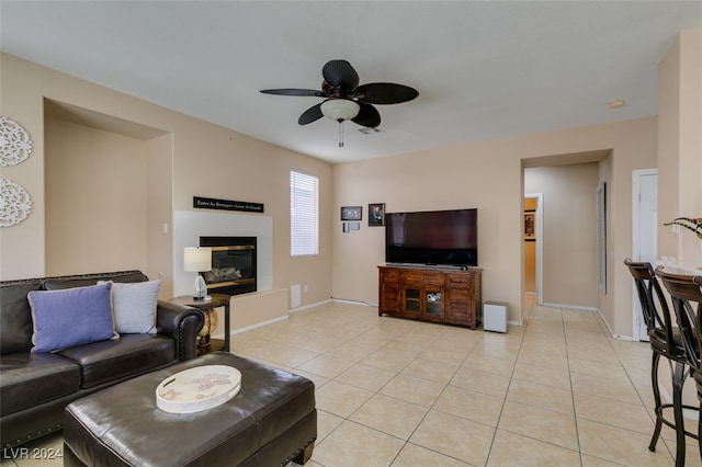 living room featuring a tiled fireplace, ceiling fan, and light tile patterned floors