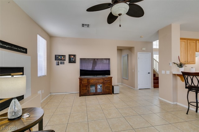 living room featuring ceiling fan, a tiled fireplace, and light tile patterned floors