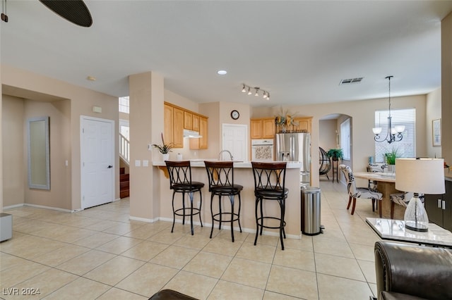 kitchen with light tile patterned floors, kitchen peninsula, a notable chandelier, a kitchen breakfast bar, and stainless steel refrigerator with ice dispenser