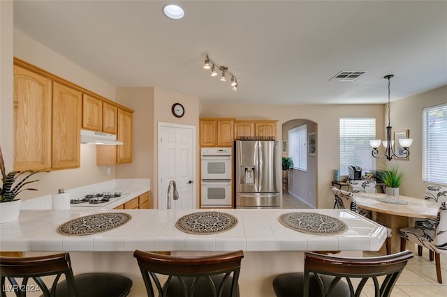 kitchen featuring white appliances, kitchen peninsula, a breakfast bar area, an inviting chandelier, and tile counters