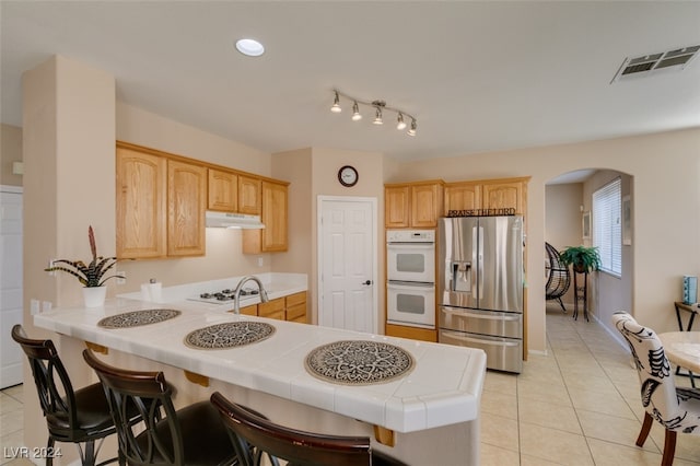 kitchen featuring kitchen peninsula, a kitchen breakfast bar, white appliances, and tile countertops