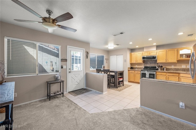 kitchen with ceiling fan, light brown cabinets, stainless steel stove, range hood, and light colored carpet