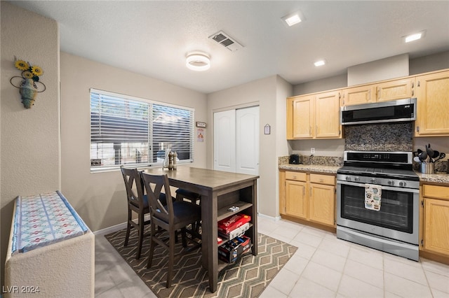 kitchen featuring light brown cabinetry, light tile patterned flooring, stainless steel appliances, and backsplash