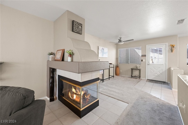 living room with light tile patterned flooring, a multi sided fireplace, a textured ceiling, and ceiling fan