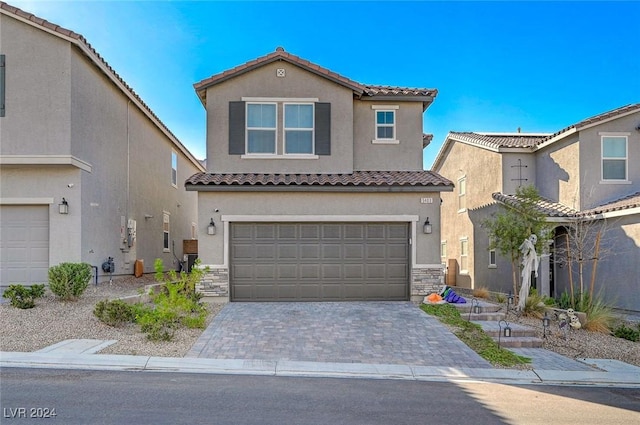 mediterranean / spanish-style home with stucco siding, decorative driveway, stone siding, a tile roof, and a garage