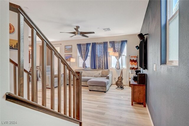 interior space featuring visible vents, light wood-type flooring, a ceiling fan, a textured wall, and stairs