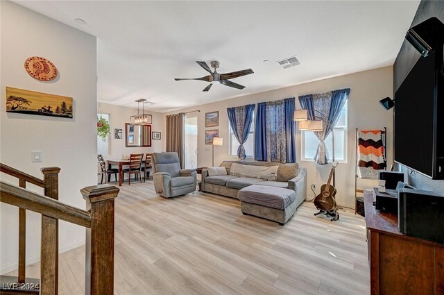 living area featuring light wood-style floors, visible vents, ceiling fan with notable chandelier, and baseboards