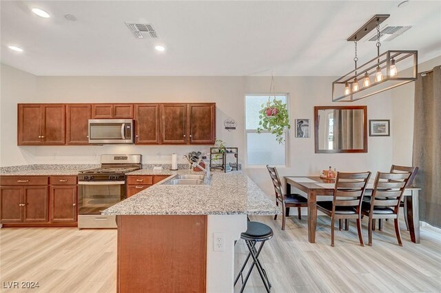 kitchen with stainless steel appliances, a peninsula, light wood-style flooring, and a sink