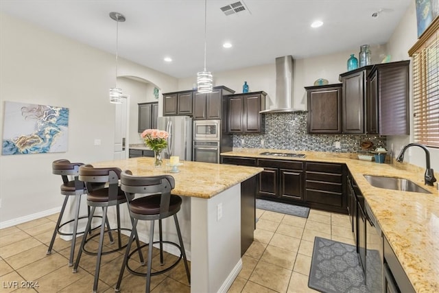 kitchen with a kitchen island, wall chimney exhaust hood, sink, pendant lighting, and appliances with stainless steel finishes