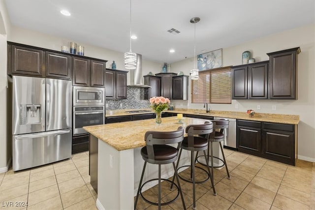 kitchen with a kitchen island, stainless steel appliances, wall chimney exhaust hood, sink, and hanging light fixtures