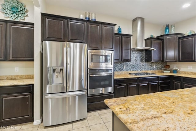 kitchen featuring wall chimney range hood, dark brown cabinetry, decorative backsplash, appliances with stainless steel finishes, and light tile patterned floors