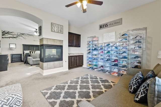 living room with a tiled fireplace, ceiling fan, and light colored carpet