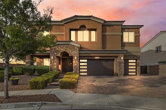 view of front facade featuring a garage, stone siding, decorative driveway, and stucco siding