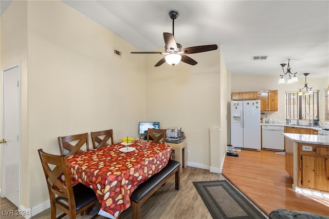 dining space featuring ceiling fan with notable chandelier, light wood-type flooring, and sink