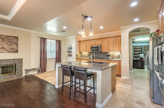 10909 Bramante Dr, Las Vegas, NV 89141 - kitchen featuring an island with sink, dark stone countertops, crown molding, stainless steel microwave, and decorative backsplash