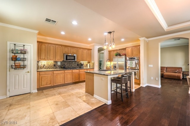 kitchen with stainless steel appliances, arched walkways, a kitchen island with sink, and visible vents