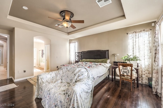 bedroom with a tray ceiling, arched walkways, visible vents, dark wood-type flooring, and baseboards