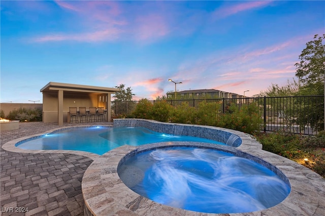 pool at dusk featuring an in ground hot tub, a patio, and pool water feature