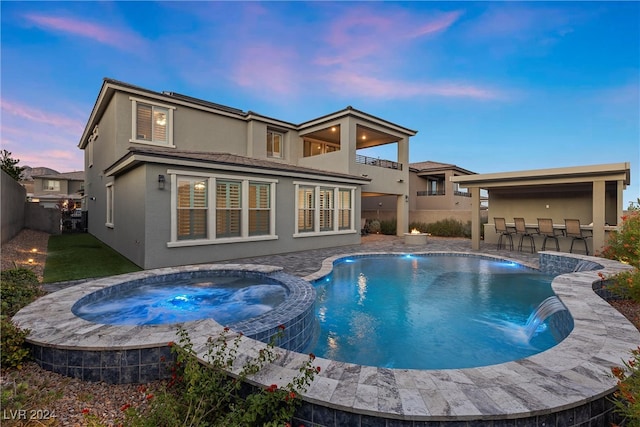 pool at dusk featuring an in ground hot tub, a patio, and pool water feature