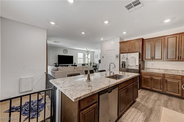 kitchen featuring visible vents, appliances with stainless steel finishes, a kitchen island with sink, light wood-style floors, and a sink