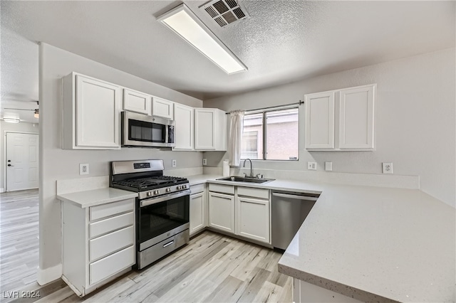 kitchen with light wood-type flooring, white cabinets, sink, appliances with stainless steel finishes, and a textured ceiling