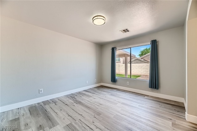 spare room featuring a textured ceiling and light hardwood / wood-style floors