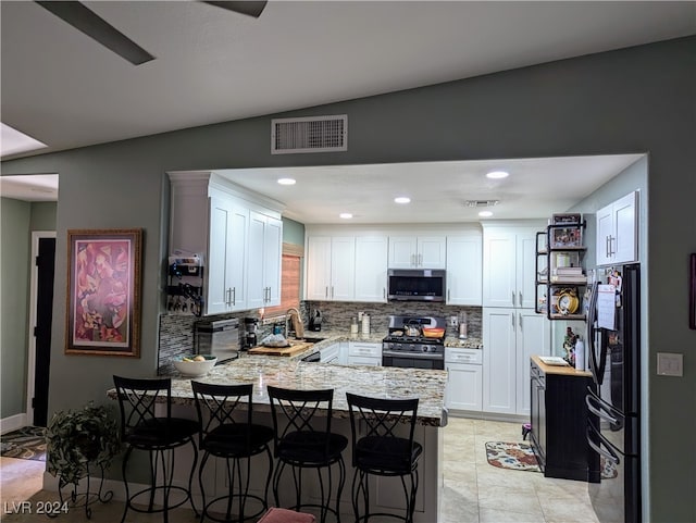 kitchen featuring kitchen peninsula, a kitchen bar, stainless steel appliances, and white cabinetry