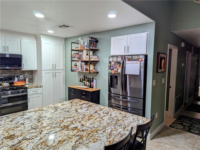 kitchen featuring white cabinets, decorative backsplash, light stone counters, and stainless steel appliances