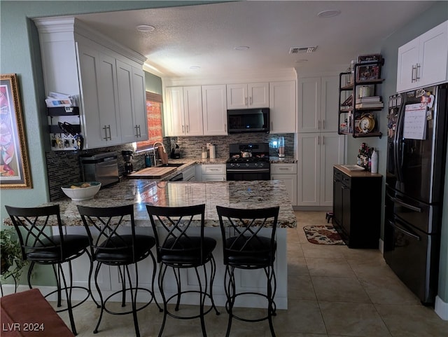 kitchen featuring stove, black fridge, light tile patterned floors, white cabinetry, and a breakfast bar area