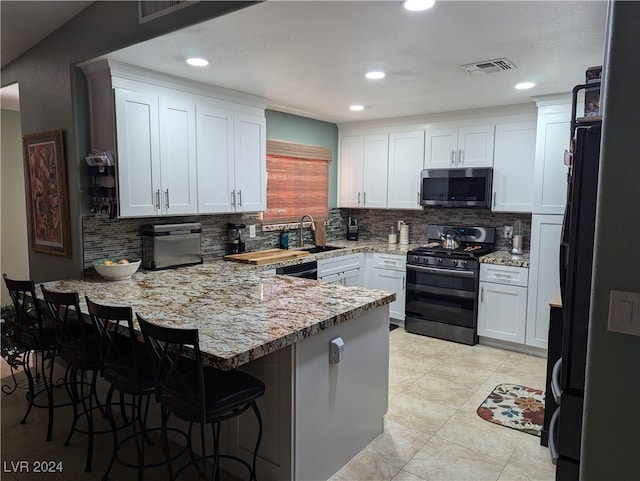 kitchen with white cabinetry, backsplash, kitchen peninsula, a breakfast bar area, and black appliances