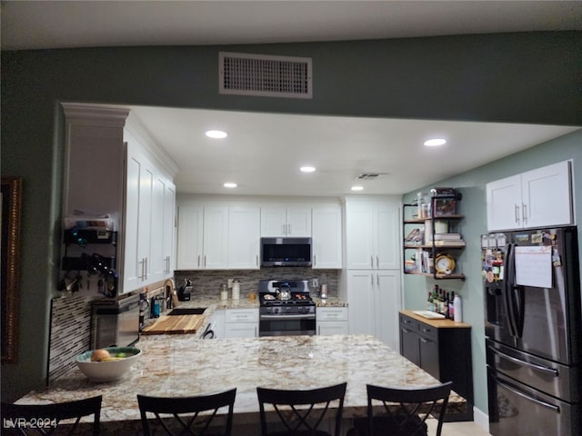 kitchen featuring kitchen peninsula, white cabinetry, light stone countertops, and appliances with stainless steel finishes