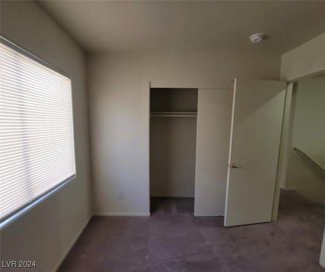 unfurnished bedroom with a closet, dark colored carpet, and multiple windows