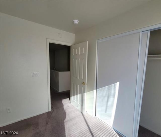 unfurnished bedroom with dark carpet and a closet