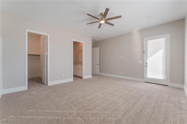 unfurnished bedroom with connected bathroom, a walk in closet, light colored carpet, a closet, and ceiling fan