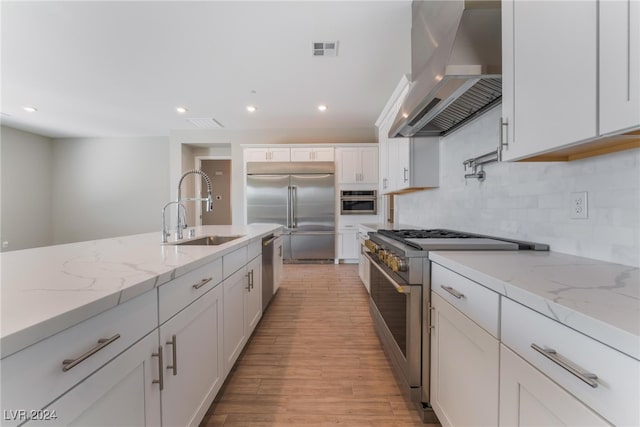 kitchen featuring ventilation hood, white cabinetry, high quality appliances, sink, and light stone counters