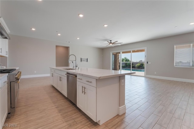 kitchen with appliances with stainless steel finishes, white cabinetry, sink, a kitchen island with sink, and light stone counters