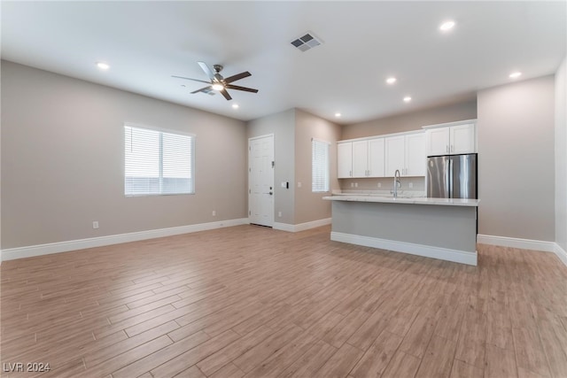 kitchen with sink, stainless steel fridge, an island with sink, light hardwood / wood-style floors, and white cabinets