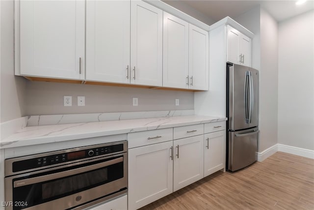 kitchen featuring white cabinetry, stainless steel refrigerator, light stone countertops, oven, and light hardwood / wood-style floors