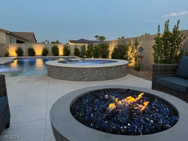 pool at dusk featuring an in ground hot tub, pool water feature, a patio area, and a fire pit