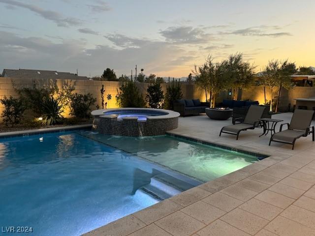 pool at dusk featuring a patio, pool water feature, and an in ground hot tub