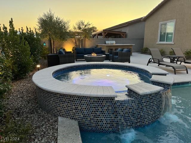 pool at dusk featuring a patio area, an outdoor living space with a fire pit, and an in ground hot tub