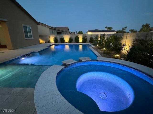 pool at dusk featuring an in ground hot tub